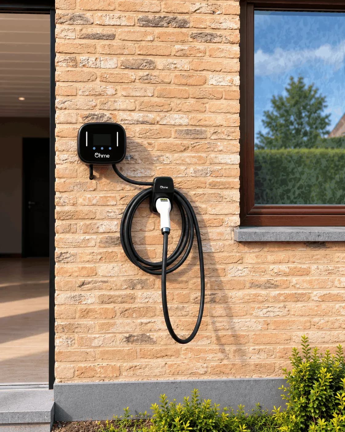 Borne de recharge Ohme installée sur une façade en briques beiges, avec câble de recharge et support mural