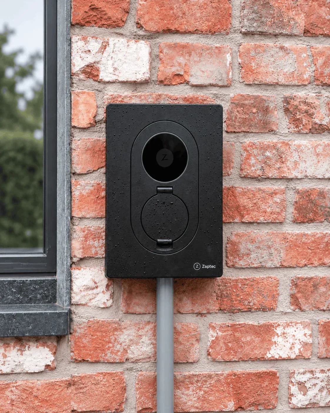 Installation murale d'une borne de recharge Zaptec noire sur une façade extérieure en briques rouges et blanches