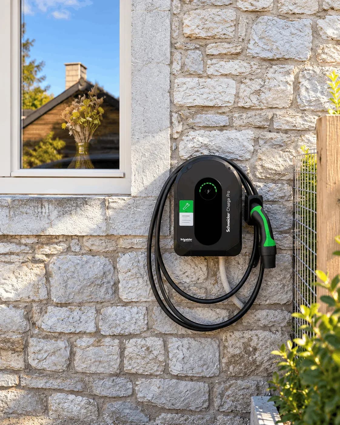 Façade en pierre équipée d'une borne Schneider Charge Pro, câble de recharge enroulé